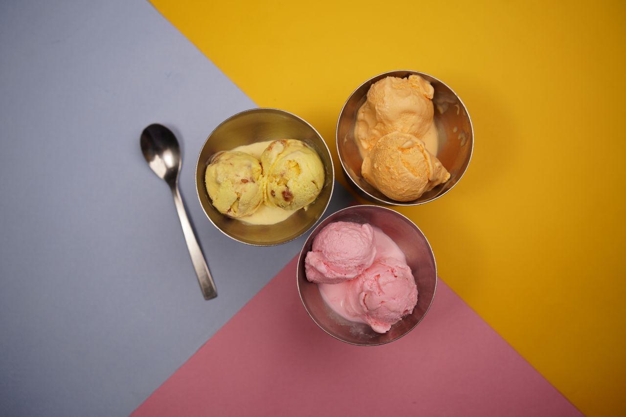 Vibrant ice cream scoops in metal bowls on colorful background.