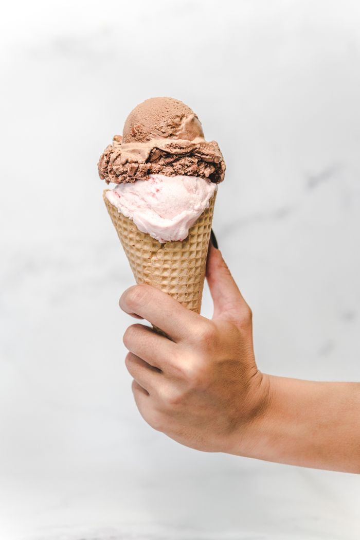 Close-up of a creamy chocolate and strawberry ice cream cone being held.
