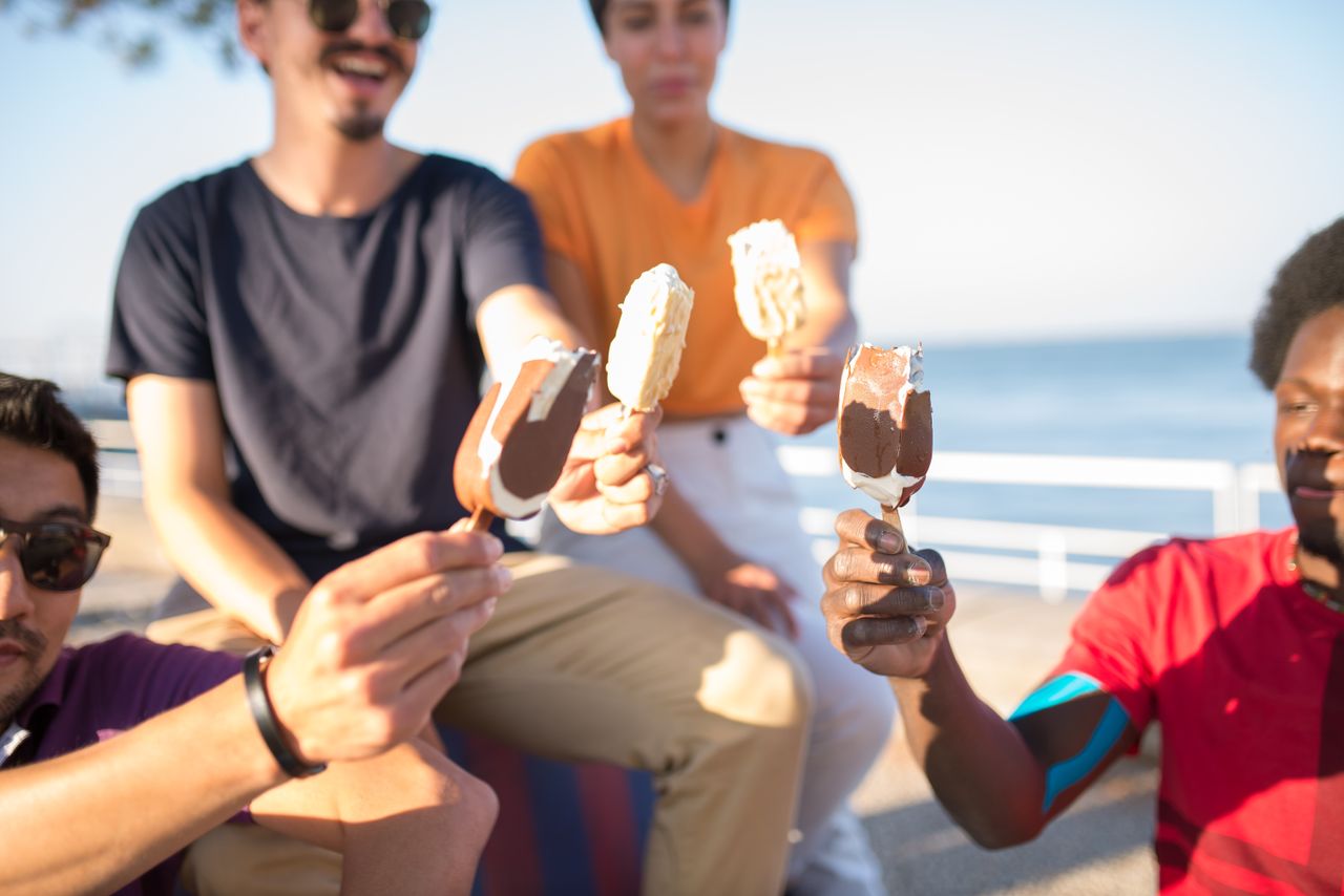 Services Group of friends enjoying ice cream bars near the ocean on a sunny day in Portugal.